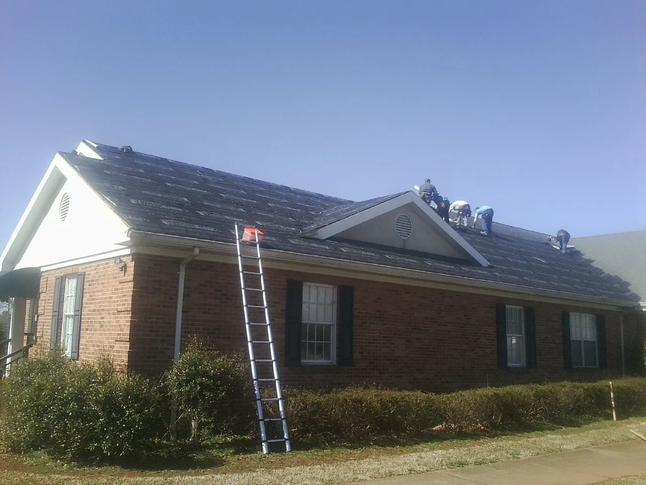 Crew tearing shingles off a brick ranch roof with a ladder set — Metal Roof Repair work by our crew in Terrell